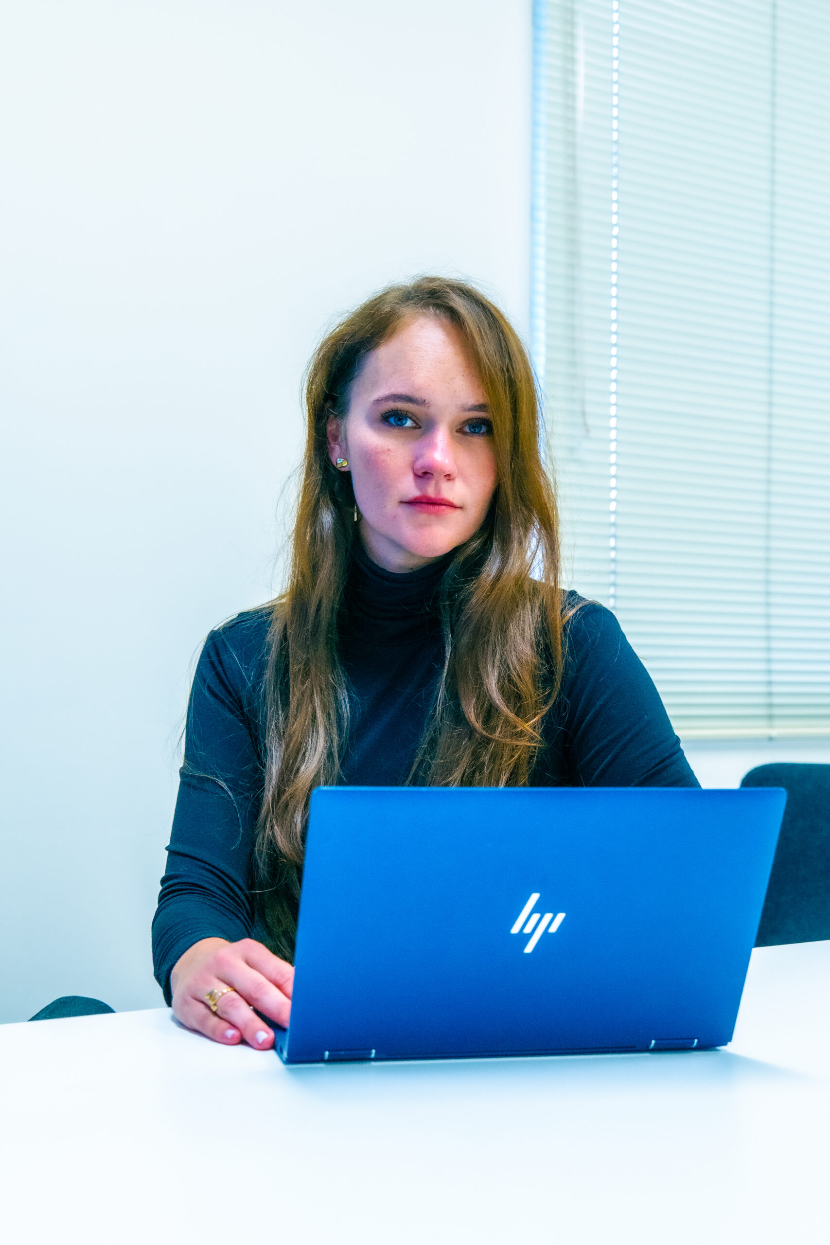 Portrait of Olga Burtseva seated in the boardroom facing the camera behind an open HP laptop.